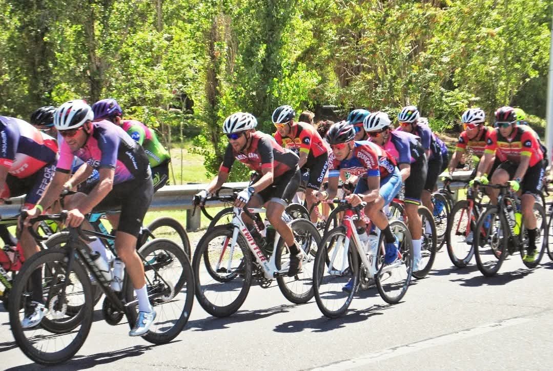 Pelotón de ciclistas avanzando por una ruta arbolada de San Juan